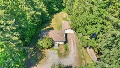 Captured from above, this property showcases a large gravel driveway, abundant land, and mature trees that provide privacy and a serene natural setting