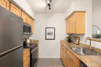Efficient galley kitchen with warm wood cabinetry, granite counters, and updated stainless appliances.