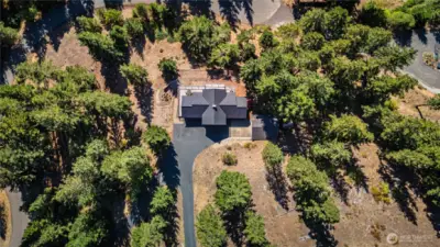 Aerial view of the home & garage. Garage has vehicle pull-up doors on both ends, a side door, & a work bench.