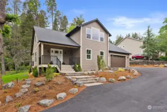 Brand new home with blacktopped driveway, professionally landscaped and hardscaped front yard in Northwest style with pavers, boulders and evergreens.