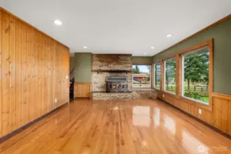 A warm and inviting living room featuring beautiful hardwood floors, warm real wood plank walls and a classic fireplace with insert that creates a focal point for your decorating and beautiful views over the back yard.