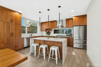 Chef’s island kitchen features rich walnut cabinetry, quartz slab counters, & high-end stainless-steel appliances