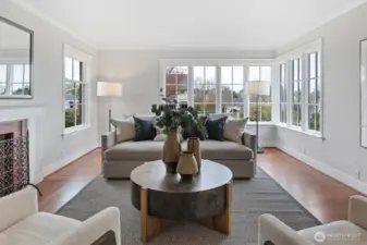 This east-facing living room is bathed in natural light, with additional southern exposure offering a view of Mt. Rainier. A wall of custom wood-clad Marvin windows—designed to echo elements of the original build—frames the view with classic divided-light detailing. Soft neutral tones, hardwood floors, and crown molding add timeless elegance, creating an ideal setting for both relaxed mornings and refined entertaining.