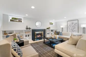 The lower-level family room offers a warm and inviting retreat, centered around a sleek gas fireplace flanked by built-in shelving. With recessed lighting, ample seating, and natural light from above-grade windows, it’s the perfect space for relaxed gatherings or cozy evenings in.
