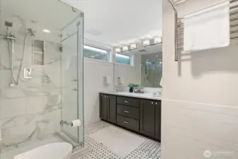 The lower-level bath is beautifully appointed with dual undermount sinks set in a durable, eco-friendly Cambria Quartz vanity. A Robern medicine cabinet, wall-mounted toilet, and heated marble mosaic tile floor elevate both function and style. The luxurious steam shower, enclosed in glass, features porcelain tile with a built-in bench and Grohe polished chrome showerhead and handheld. A heated towel rack completes the spa-like experience.