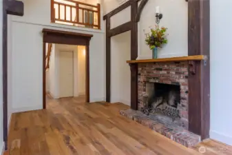 Charming Tudor-style living space featuring rustic wood beams, a brick fireplace with timber mantel, and warm hardwood floors—blending old-world character with cozy elegance.
