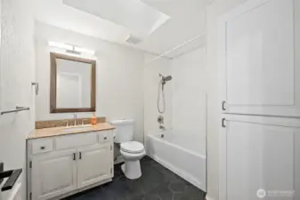 Black hexagon tile floor in full bathroom with storage cabinets inset into wall. Skylights bringing in extra light.