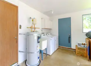 Garage with new electric water heater - just installed in December, 2024. Also washer and dryer along with utility sink and cupboards are here in the attached garage, along with an EV charging outlet!