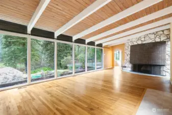 Living room with curved stone and brick fireplace and window wall overlooking Issaquah Creek