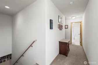 At the top of the stairs, the bedrooms are separated with the primary on the left (behind the photographer in this frame) and the other two bedrooms on the right, down this hallway and around the corner.