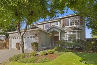 Charming curb appeal with mature landscaping, brick accents, and a welcoming covered entry.