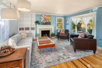 Living room features wood burning fireplace, built in book shelves, and large bay window