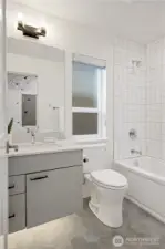 Entry level guest bathroom with hexagon tile heated floors, floating vanity with under mount accent lighting, and full tile surround with bathtub.