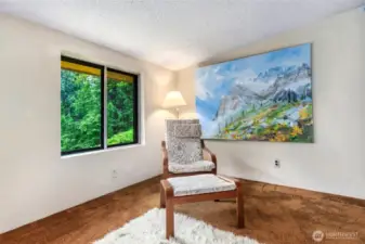 This inviting corner of the upper-level primary suite offers a peaceful spot to relax, with a large window framing views of lush greenery.