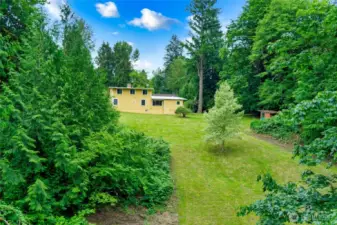 The land behind the home offers a peaceful blend of open lawn and wooded privacy. A well-kept grassy area stretches out from the house, anchored by a single tree that adds charm and shade. Beyond that, clusters of mature trees and shrubs create a natural backdrop—perfect for quiet walks, gardening, or simply enjoying the view. It’s a serene setting with plenty of space to explore, relax, and connect with nature.