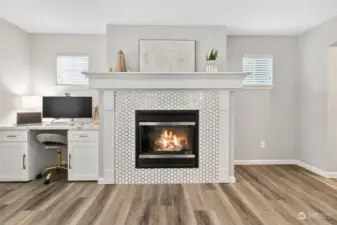 Embrace comfort and elegance with a cozy gas fireplace framed by exquisite tile work and a sturdy mantel, creating a captivating focal point.  Off to the side is a functional and beautiful built in desk with an exquisite quartz called Calcutta Goid.