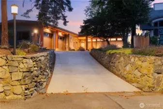 Sunset view of the home from the street with beautiful rock wall work and under lighting.