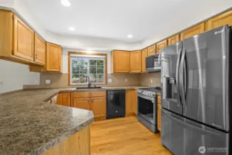 Kitchen with granite countertops, stainless steel appliances, ample cabinetry, and window above the sink overlooking the backyard.