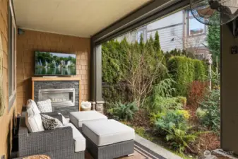 Covered patio with a mounted TV, fireplace, and motorized shades
