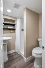 A full bathroom upstairs with laminate flooring, shelves, shower, ceramic pedestal sink & a toilet.