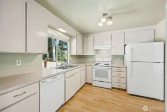 Cute kitchen with laminate flooring and a window looking out over the park-like back yard.