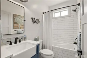 The shared bath features striking white subway tile paired with custom ceramic tile flooring, creating a clean and timeless finish.