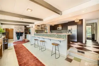 Step into retro-modern elegance! This open-concept kitchen features custom mosaic tile, a spacious breakfast bar, and rich wood cabinetry—all flowing seamlessly into the vibrant living area with exposed beams and a cozy stone fireplace. Perfect for entertaining in style or enjoying quiet moments at home.