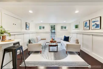 Basement rec room at bottom of stairs with wainscoting and a stylish glass door out to the back yard.