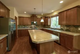 This kitchen sold the current owner!  Large island with tile countertop and tile countertops with tile backsplash and rich wood cabinetry, pendant lighting, newer stainless appliances and large walk-in pantry makes this a delightful place to prepare meals