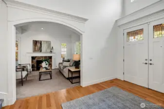 The light-filled entry opens gracefully to the formal living room through a wide arched doorway, showcasing elegant millwork, a cozy fireplace, and a welcoming ambiance perfect for entertaining.