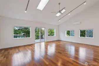 Spacious, light-filled open Great Room / Living Room / Dining Room with west-facing view to deck and lake beyond. Brazilian hardwood floors, vaulted ceiling, skylights, ceiling fan, track lighting, air conditioning / heat pump split system.