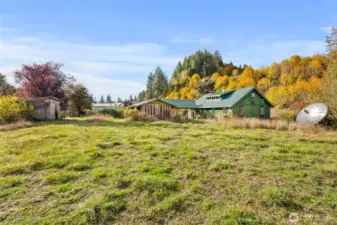 Backyard view to back of house, woodshed, garden shed, and barn in far background.