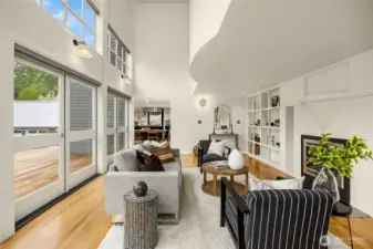 The livingroom sheltered by a bowed fronted balcony (mezzanine above) is centered on the fireplace and flanked by an abundance of bookshelves and grounded by polished wood floors.