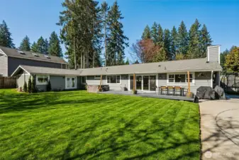 From this corner angle, the home really stretches out and shows off its true rambler layout. The L-shaped design creates natural zones in the backyard, giving you separate areas for relaxing, playing, and entertaining without everything feeling piled into one spot. You can see the French doors leading into the primary suite on the left, which adds a nice private connection to the outdoor space, perfect for morning coffee or winding down at the end of the day. The HardiPlank siding continues across the entire back of the home, tying durability and clean design together. Between the deck, sport court, patio areas, and open lawn, this yard is set up to host everything from quiet evenings to full gatherings. It’s easy to picture this becoming the go-to house where people naturally end up.