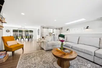 The warm-toned luxury vinyl plank flooring carries your eye straight through the living room into the dining and kitchen spaces, grounding everything with a cohesive, easy-to-live-with feel. The soft neutral palette reflects light beautifully while still adding a bit of depth and personality so it doesn’t feel flat. Off to the side, the barn-style doors to the office or den add a touch of character and flexibility depending on how you use the space. And then there’s that oversized multi-panel double sliding glass door pulling in a ton of natural light and opening the whole back of the home up to the yard.