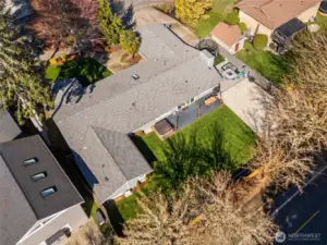 This overhead view really lets you appreciate how much is packed into this backyard, and how well it all works together. The fully fenced layout includes a huge sport court that opens the door to everything from pickup games to weekend tournaments, a hot tub included with this home is ready for evening wind-downs, and a big stretch of green lawn that actually gives you room to run, play, or just spread out. There’s even a trampoline already in place that can stay with the home too. The large deck made of easy-care composite material just off the dining room creates a natural extension for outdoor living, making it easy to move between inside and out. You can also see the roof in detail here, newer and in great shape, along with the row of mature trees just beyond the fence line that provide shade in the summer and a beautiful show of color in the fall.