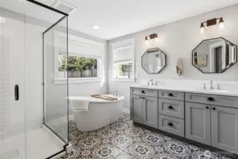 The patterned black and white flooring in the primary suite bathroom gives it that modern boho edge without overpowering the space, and everything else balances it out beautifully. There’s a low-threshold glass shower for easy entry, plus a separate soaking tub that feels like a true retreat feature. The double vanity with gray shaker cabinets offers plenty of storage, and the octagon beveled mirrors bring in a bit of character without going over the top. Subway tile keeps the look grounded, while the corner windows above the tub add natural light with privacy shades already in place.