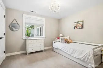 This bedroom has a softer, more playful personality to it with the delicate chandelier with glass crystal details adding just a hint of sparkle, giving the room a little charm without feeling over the top. The warm fawn, latte-toned walls paired with plush carpeting create a cozy, pulled-together feel that’s easy to settle into. White trim keeps everything crisp and balanced, and the window looking out to the backyard brings in natural light while keeping the setting calm and private. It’s a sweet, comfortable space that works well for a bedroom, guest room, or anything in between.