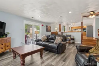Lower-level living space w/ slider to the outdoors & clear sightlines toward the dining area & kitchen—blending indoor comfort w/ seamless flow.