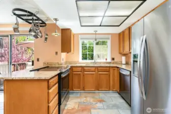 Kitchen features matching appliances, natural cabinets, peninsula, and window above the sink.