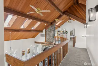 Catwalk view showcases the stunning vaulted ceiling with rich wood detail & skylights that pour in natural light—perfectly framing the grandeur of the 2-story river rock fireplace below