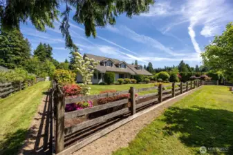 Split rail fence borders the front yard, gracefully defining the garden area—adding charm, structure & a classic touch to the beautifully landscaped entry
