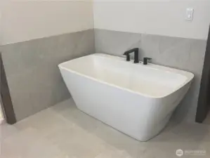 Primary bath has a deep free standing tub surrounded by a tile wainscot wall.