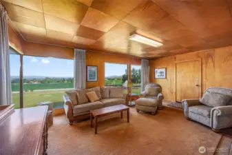 This cozy living room features classic wood paneling and floor-to-ceiling windows, bringing in plenty of natural light and offering a glimpse of the old-time charm. A perfect space to relax and enjoy the nostalgic atmosphere of this 1950 guest house.