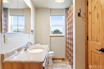 Bright bathroom with a solid wood door, mirrored storage, and a tiled shower/tub combo. Natural light from dual windows adds warmth and charm.