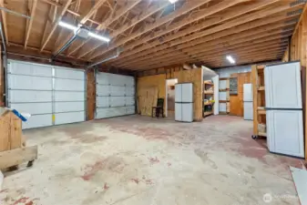 Expansive garage/shop space with double bay doors, insulated storage room, open rafters, and ample storage — perfect for vehicles, projects, or a home workshop.