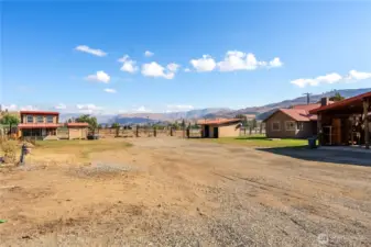 Backyard perspective showcasing multiple outbuildings, covered parking, and wide-open space for outdoor living.