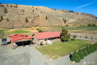 Expansive aerial shot showcasing the home, multiple outbuildings, large fenced arena, and surrounding open land.