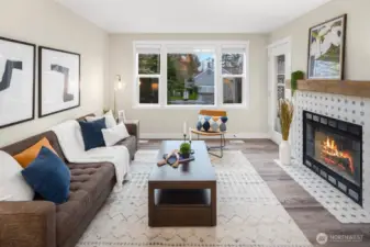 Large living space, with luxury vinyl flooring, wood-burning fireplace with reclaimed wood mantel and Moroccan tile, ample light through a wall of windows.