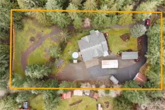 Aerial view highlighting the property boundaries and layout, showcasing the home, outbuildings, yard space, and circular driveway.